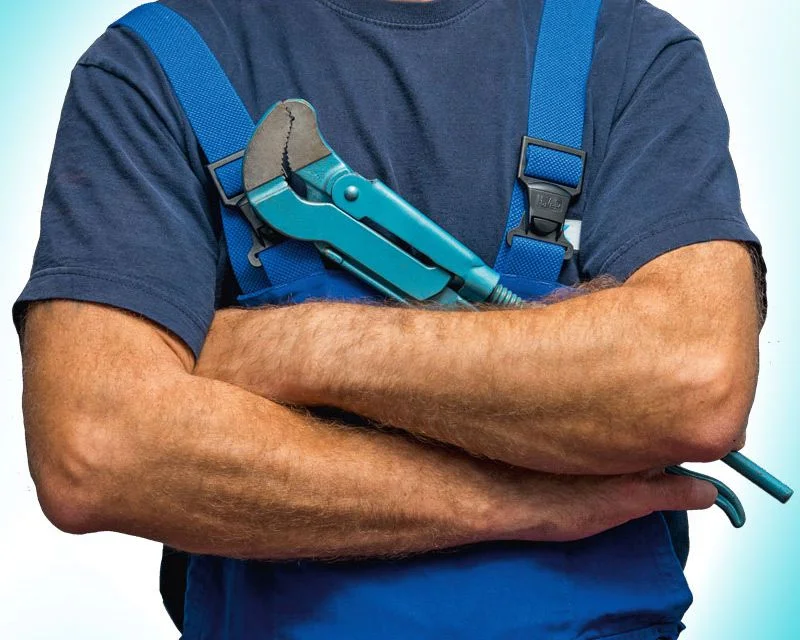 Ein Sanitärinstallateur in Arbeitskleidung hält eine Rohrzange vor der Brust.