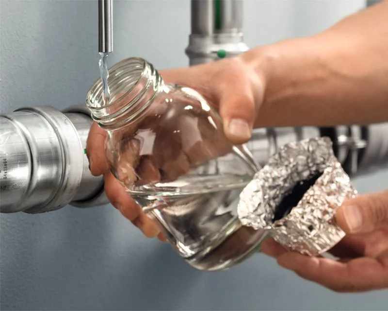 Eine Hand füllt Wasser aus einer Leitung in eine Glasflasche.